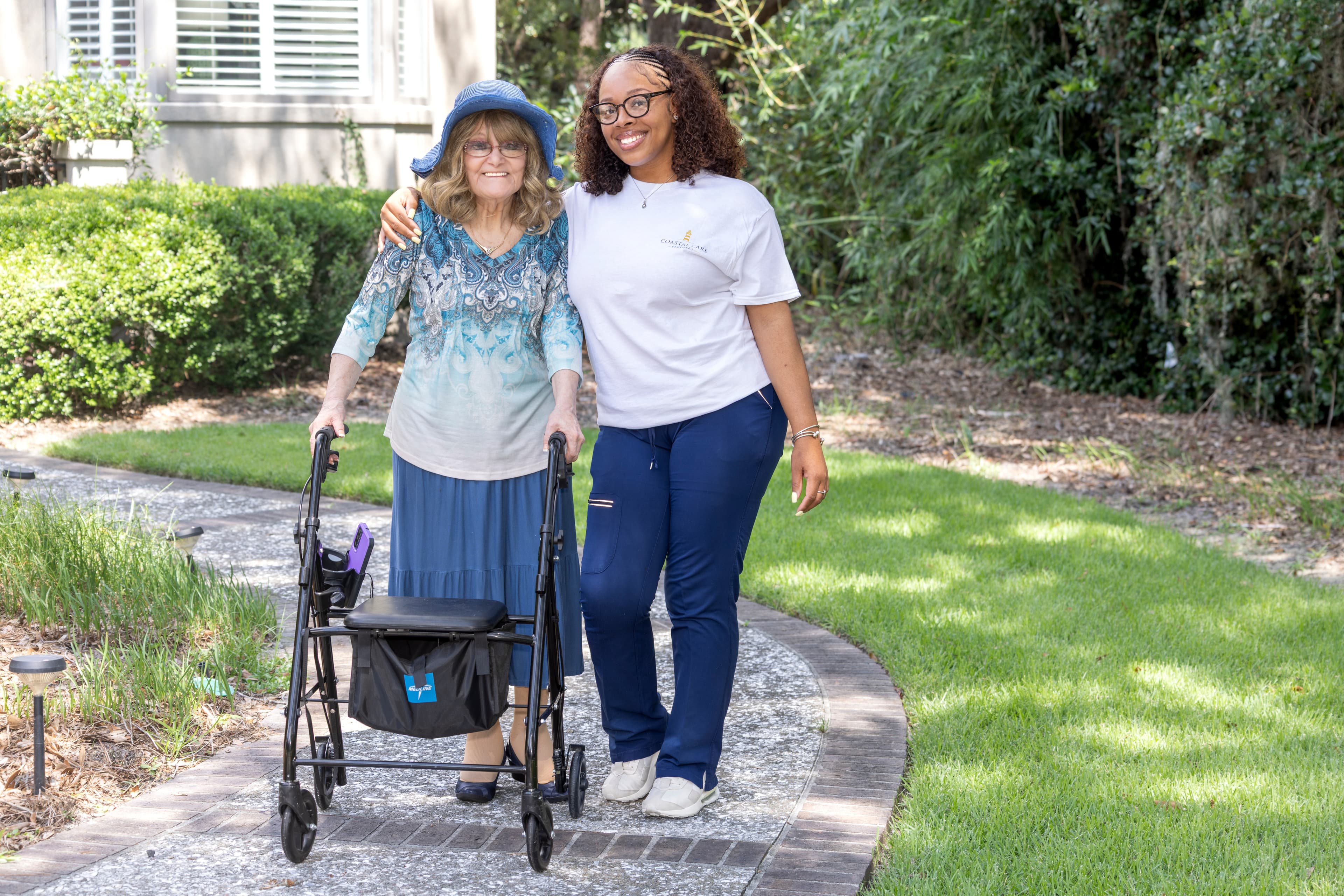 Caregiver assisting elderly client with walker on an outdoor pathway
